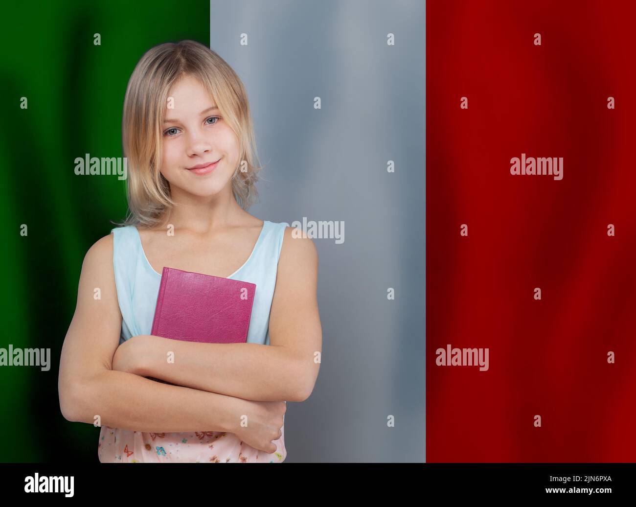 Ragazza carina piccola allegra con libro sullo sfondo della bandiera italiana. Impara il concetto di lingua italiana. Foto Stock
