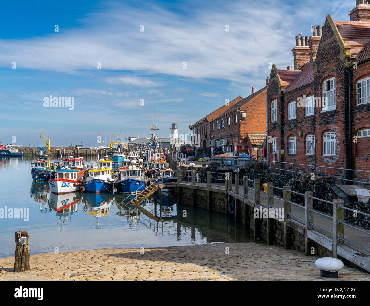 Scarborough, Regno Unito - 16 giugno, 2022: Barche da pesca colorate e pescherecci da traino accanto al porto in mattoni rossi nel porto turistico e nel porto di Scarb Foto Stock