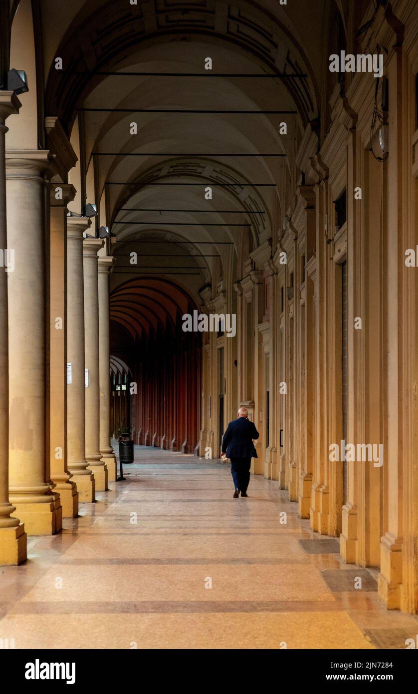 Vecchio in tuta nera che cammina all'ombra nelle calde giornate estive a Bologna Foto Stock