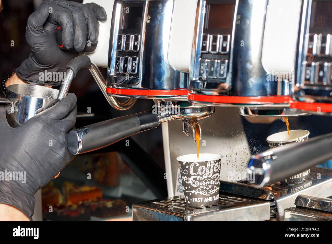 Le mani del barista in guanti in lattice nero preparano il caffè caldo in una macchina da caffè. Foto Stock