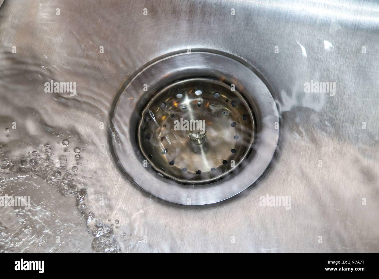 Lavello in acciaio inox con tappo di scarico e acqua corrente - primo piano Foto Stock