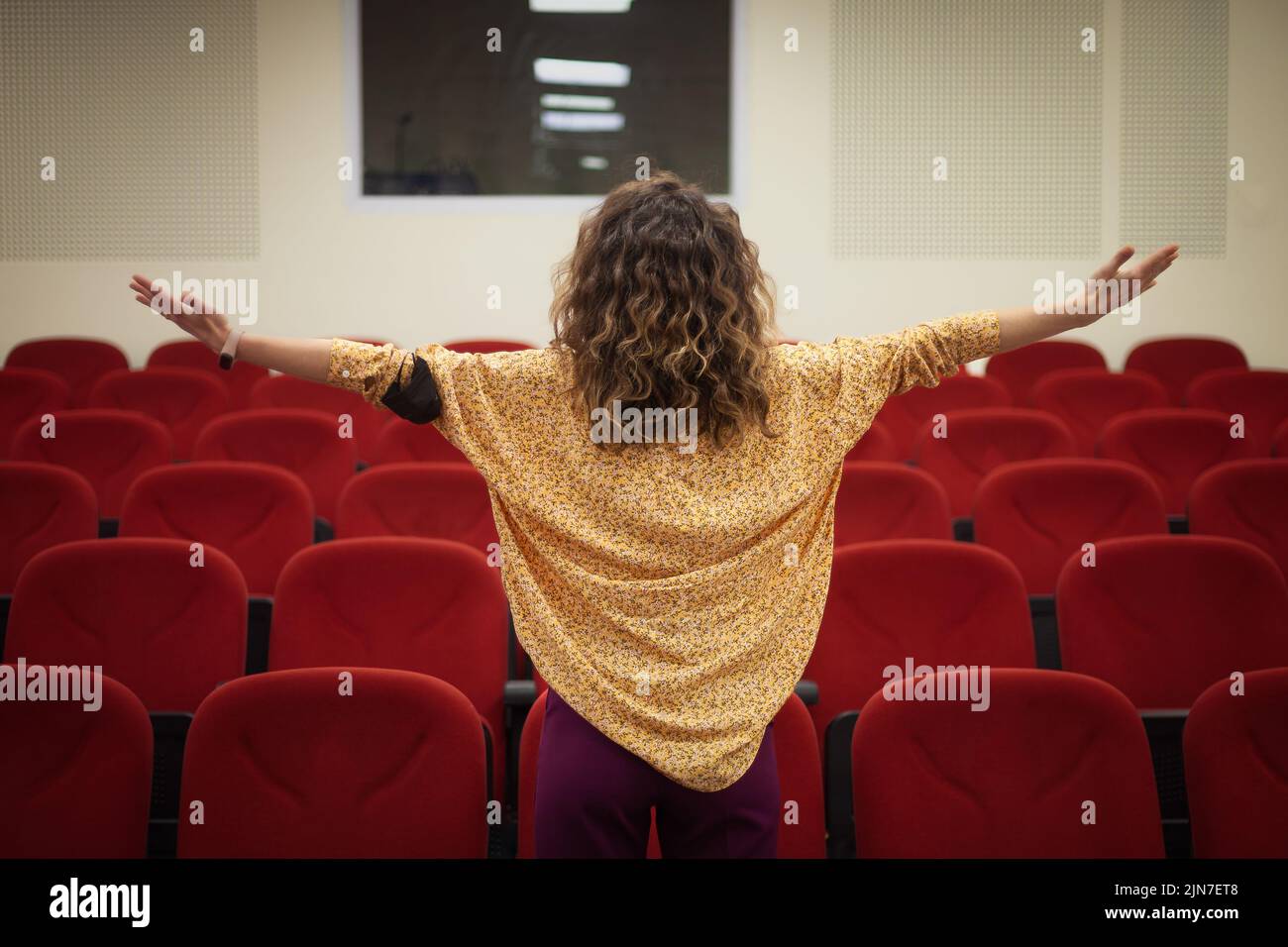 Donne in piedi davanti alle poltrone rosse. Donna che apre le mani in un cinema vuoto Foto Stock