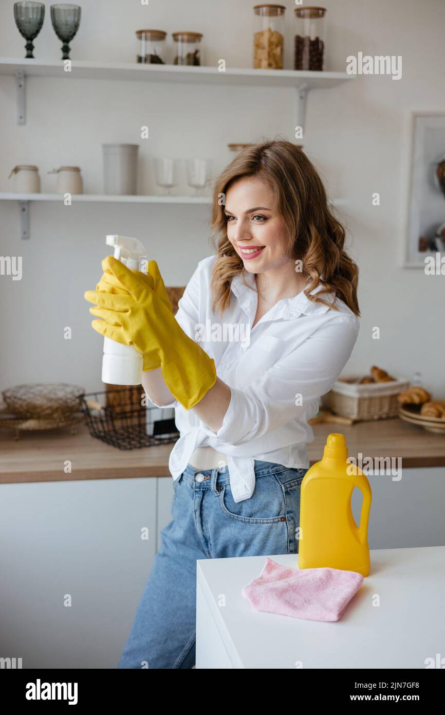 Una ragazza in guanti gialli tiene uno spray detergente sullo sfondo della cucina Foto Stock