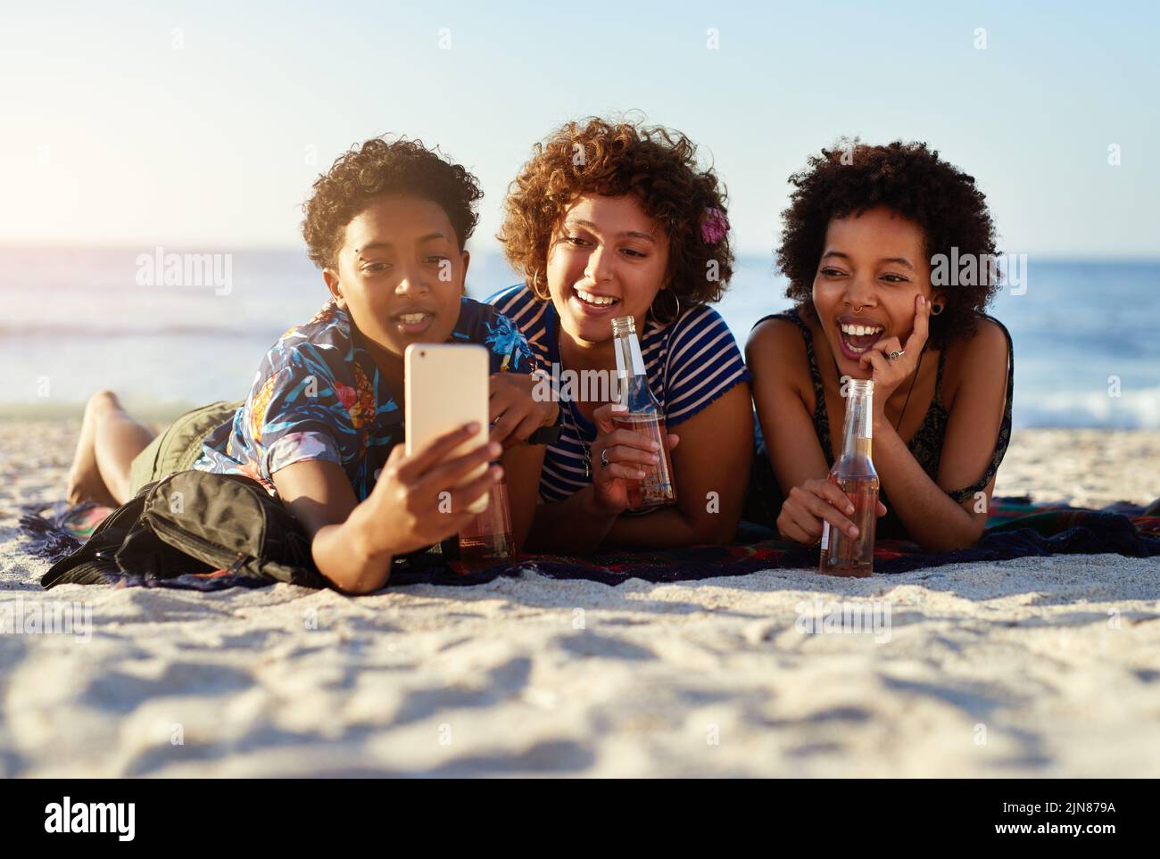 Ricordiamoci questo momento per sempre. Un attraente trio di donne che si stendono sulla spiaggia e che prendono insieme i selfie durante il giorno. Foto Stock