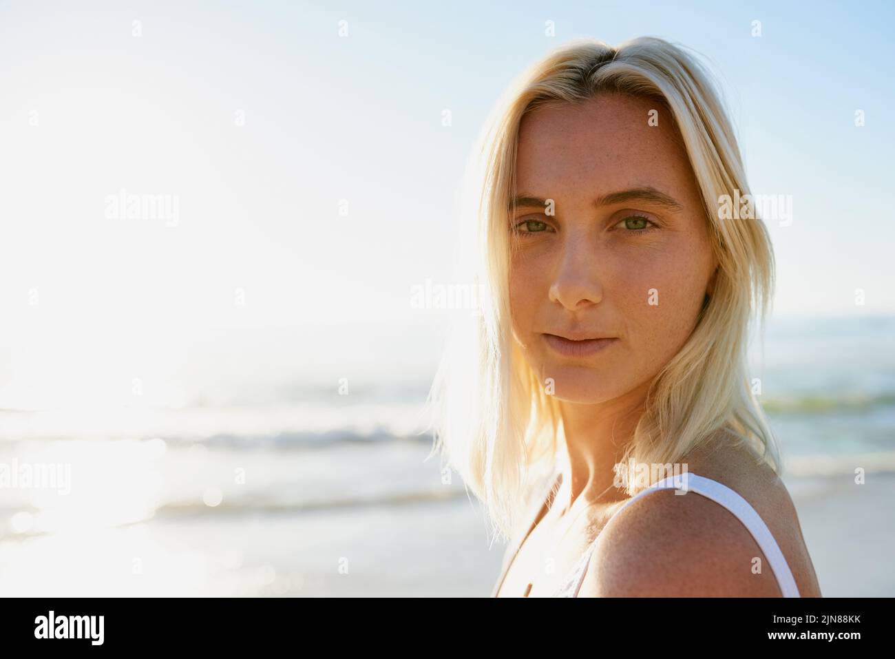 In pace con me. Ritratto corto di una giovane donna attraente che guarda sopra la sua spalla sulla spiaggia con l'oceano dietro di lei. Foto Stock