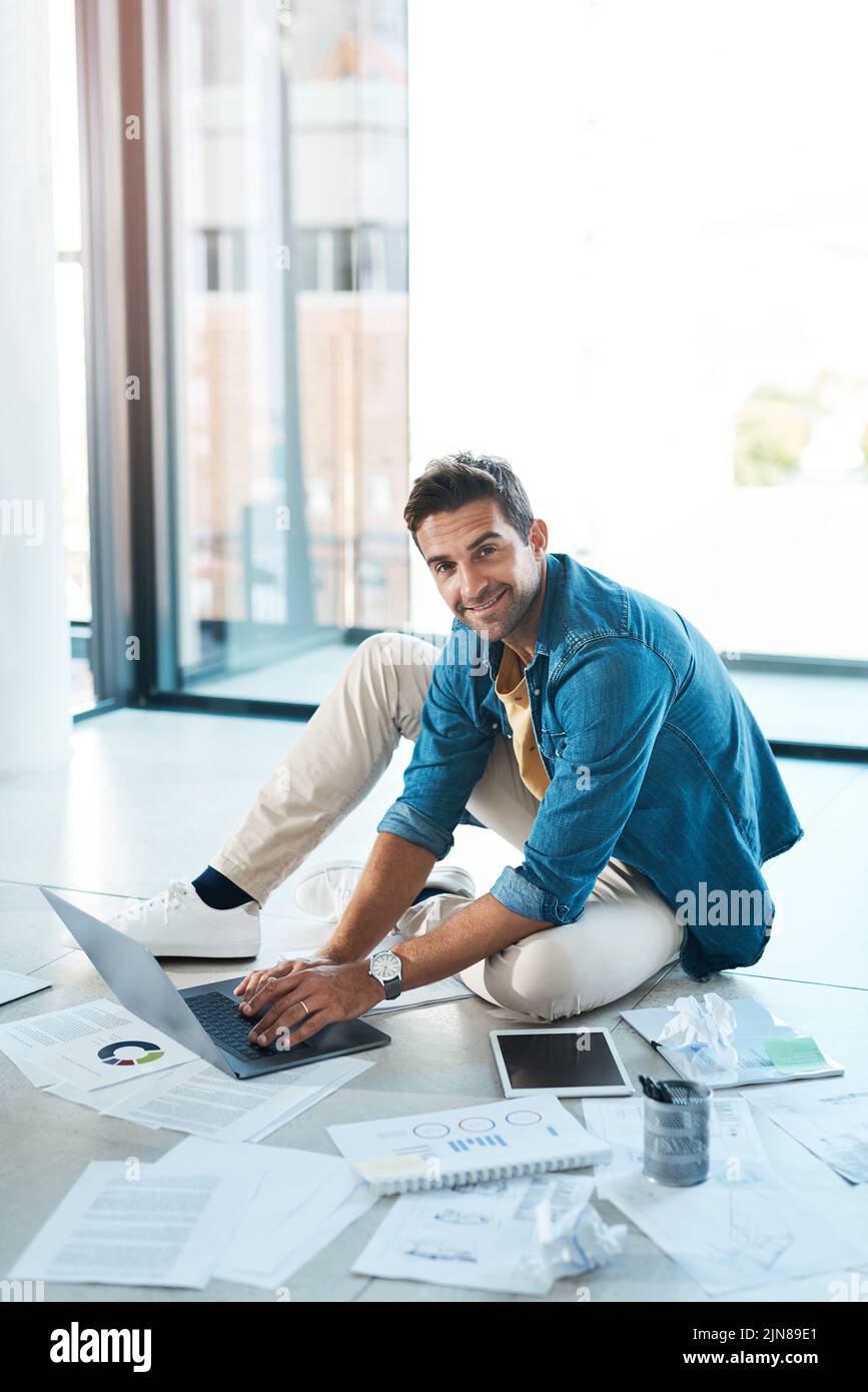 I miei piani sono solidi. Ritratto di un giovane uomo d'affari brainstorming con un laptop e documenti su un pavimento in un ufficio. Foto Stock