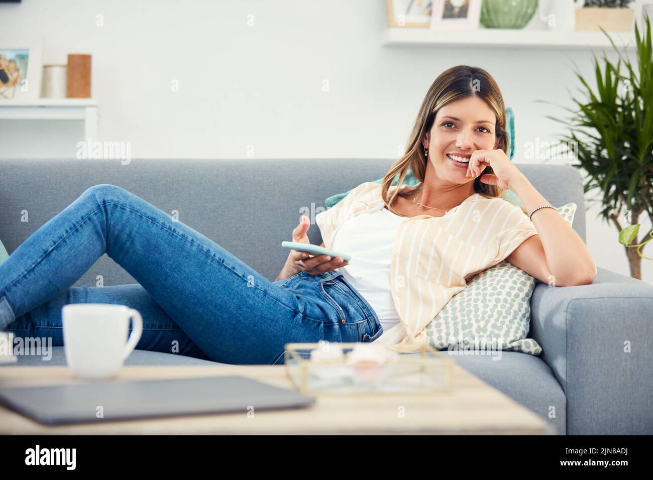 Potete trovare l'intrattenimento a portata di mano. Una donna attraente che usa il suo cellulare mentre si rilassa a casa. Foto Stock