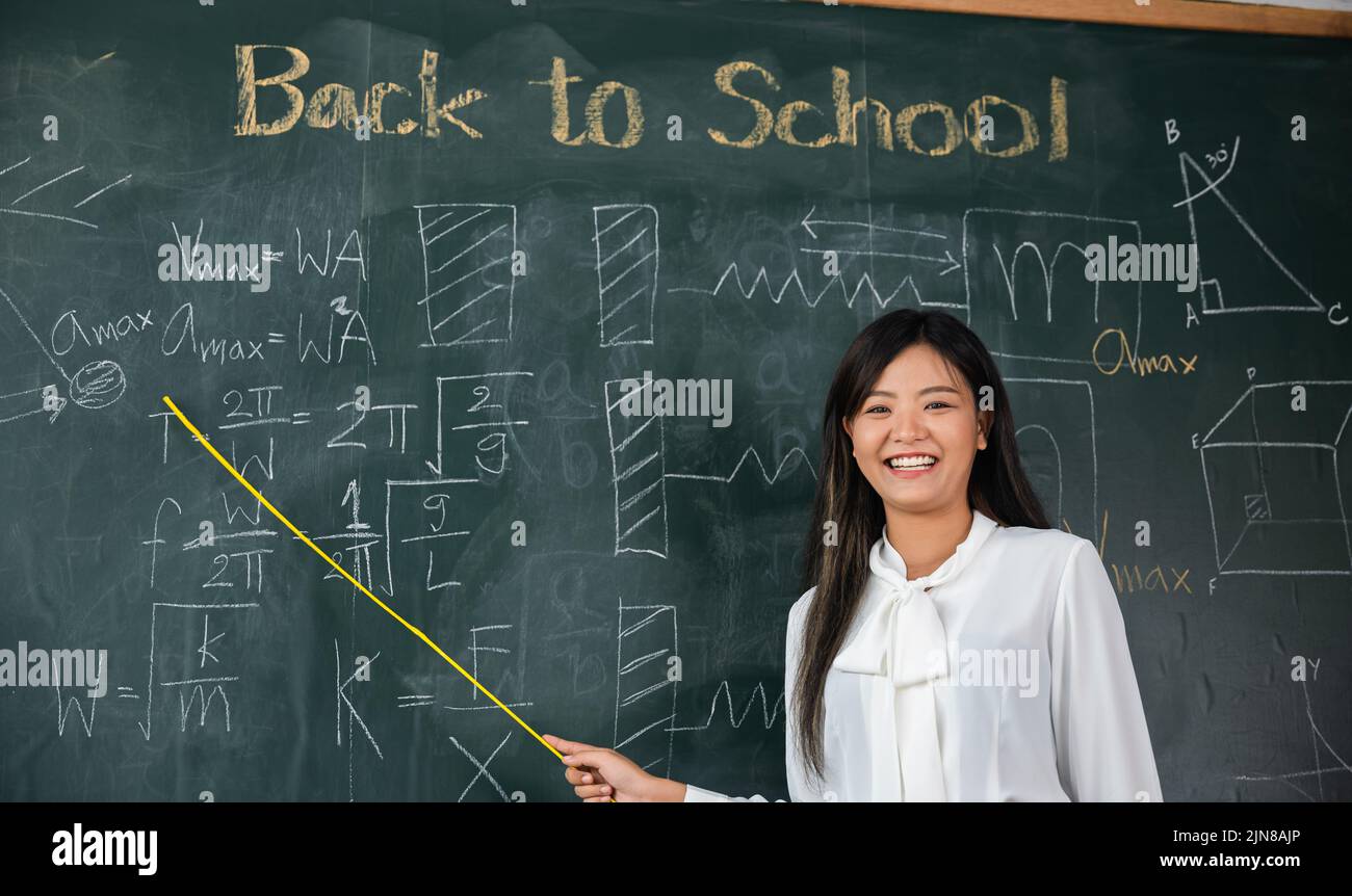Concetto di ritorno a scuola. Insegnante femminile asiatica sorridente con bastone di legno che punta alla lavagna a scuola in classe, felice bella donna stan Foto Stock