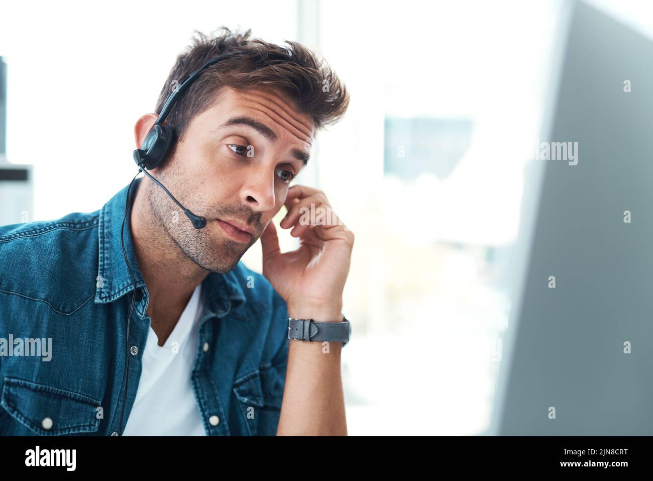 A volte i clienti possono essere molto difficili. Un giovane agente del call center che guarda turbato mentre lavora nel suo ufficio. Foto Stock