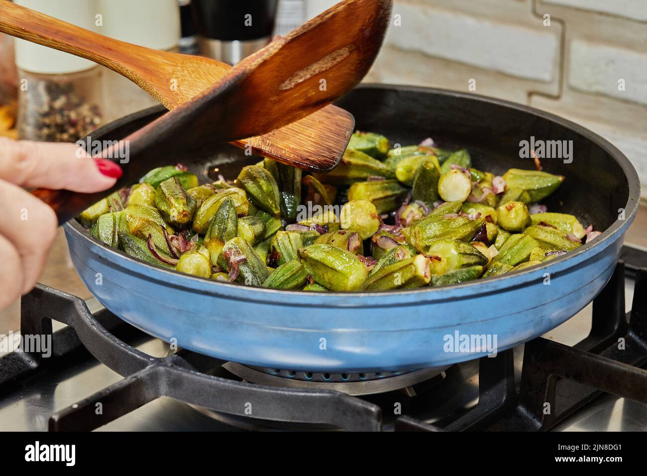 Lo chef mescola l'okra nella padella con le cipolle viola fritte Foto Stock