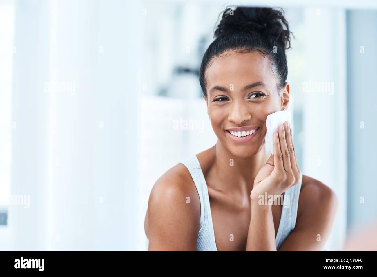 Mi piace prendersi cura della mia pelle. Ritratto di una giovane donna attraente che pulisce il suo viso con un batuffolo di cotone in bagno a casa. Foto Stock