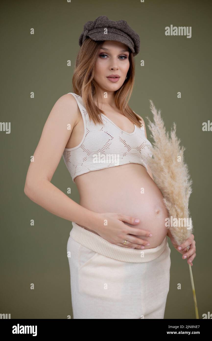 Donna incinta in abito tiene le mani sul ventre su uno sfondo bianco. Gravidanza, maternità, preparazione e concetto di aspettativa. Primo piano, spazio di copia Foto Stock