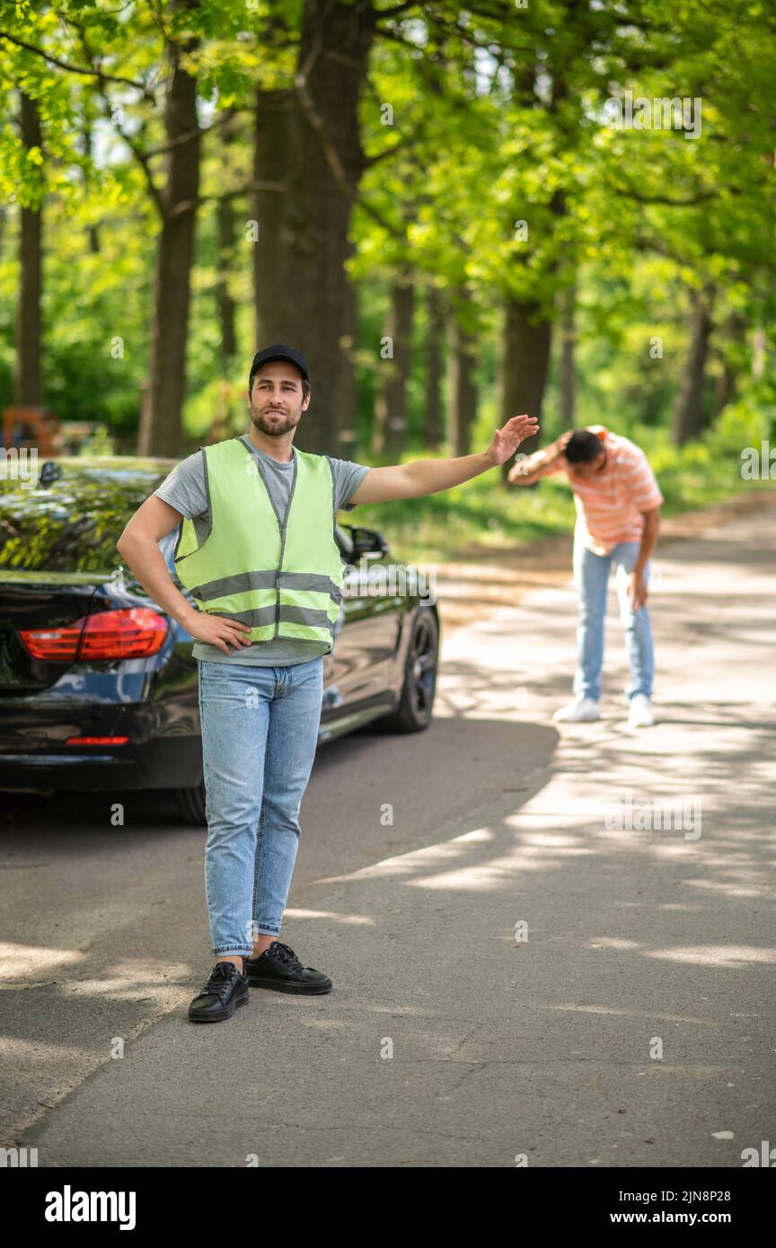 Il serviceman in un gilet giallo hitchhiking sulla strada Foto Stock