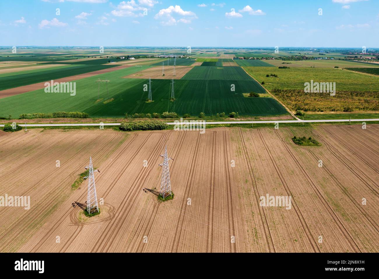 Torri di trasmissione a traliccio elettrico e linee elettriche su campo coltivato, vista ad angolo alto del drone pov Foto Stock