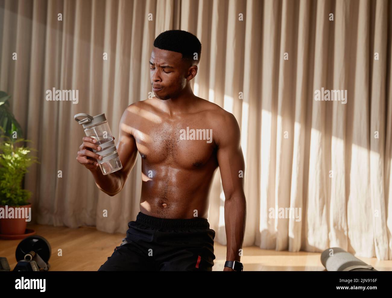 Giovane atleta afro americano nero maschio acqua potabile dopo un allenamento ad alta intensità a casa facendo una classe online. Mantenendo la forma e. Foto Stock