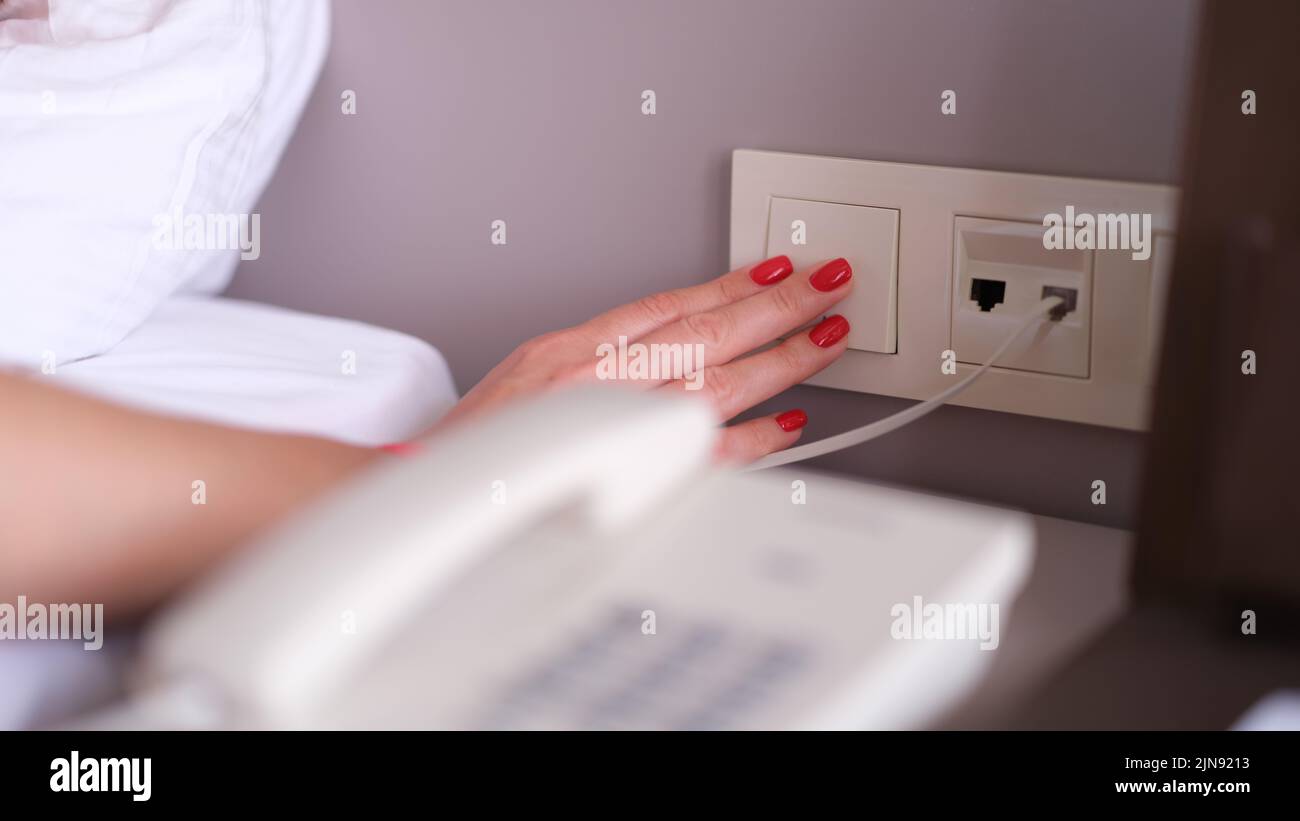 La mano della donna si spegne o accende la luce con l'interruttore bianco in primo piano Foto Stock