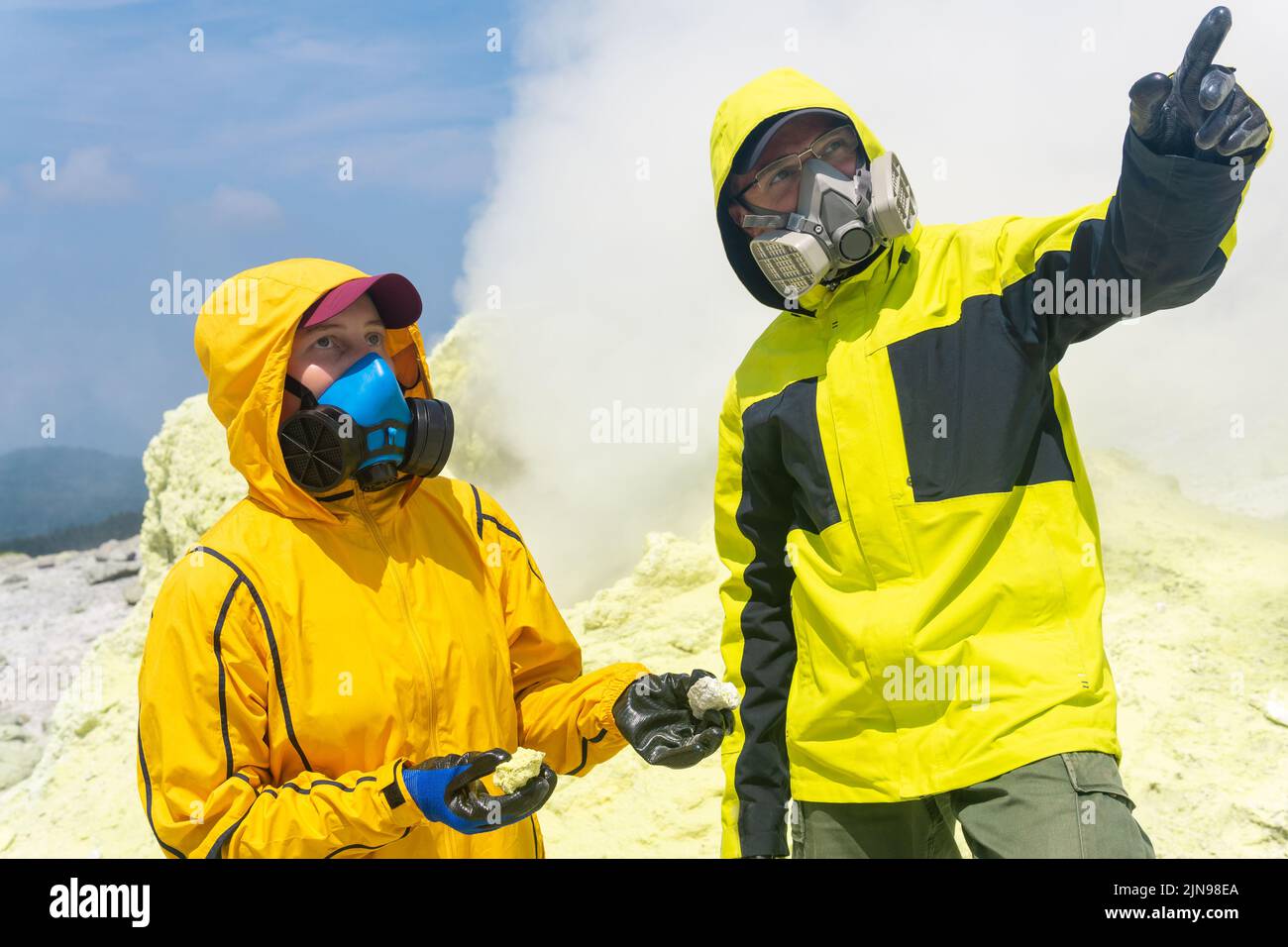 i vulcanologi sul pendio del vulcano raccolgono campioni sullo sfondo di fumarole di zolfo fumante Foto Stock