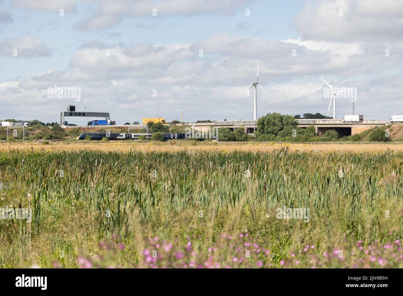Stafford-Staffordshire-Regno Unito 27 aprile 2022 paludi verdi confinano con una trafficata autostrada e linea ferroviaria, con due turbine eoliche, il clima, l'energia Foto Stock