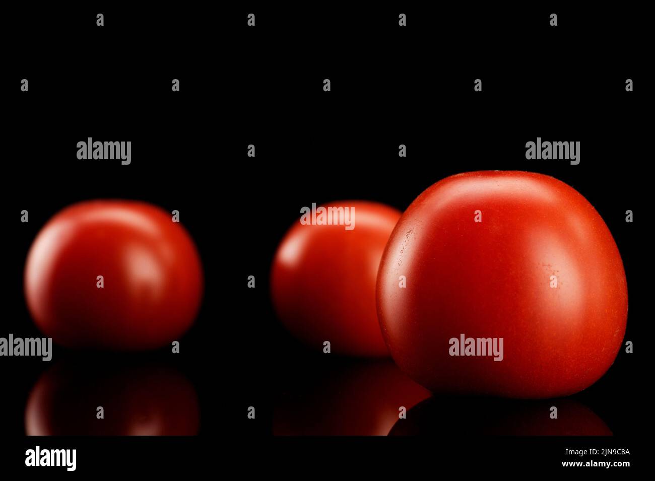 Frische rote Tomaten auf glänzendem, schwarzen, Untergrund | pomodori freschi rossi su fondo nero Foto Stock
