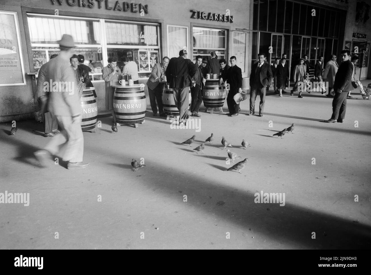 Original-Bildunterschrift: Etwas fällt immer für sie ab für die vielen Tauben, die in der Großen Bahnhofshalle des Münchener Hauptbahnhofs 'wohnen' und sich vorzugsweise in der Nähe der aus Bierfässern bestehenden Imbisstische aufhalten, München, Deutschland 1961. Foto Stock