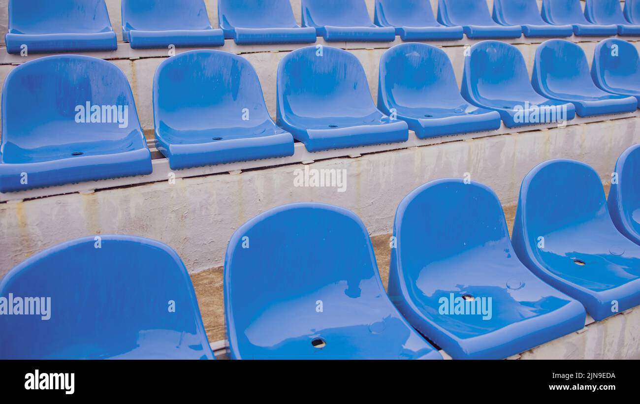 Vuoto bleacher nello stadio sportivo in tempo piovoso. Sedili colorati bagnati nello stadio di strada. Piove. Primo piano Foto Stock