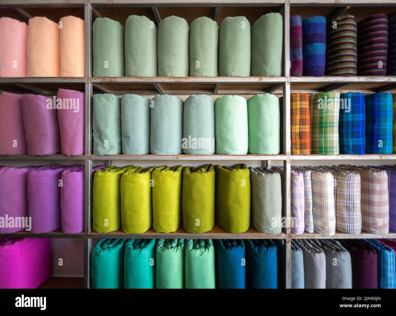 I rotoli di seta tessuta fatti a mano in tradizionale stile thailandese sono su scaffali all'interno di un negozio di abbigliamento locale in Thailandia, vista frontale con lo spazio copia. Foto Stock