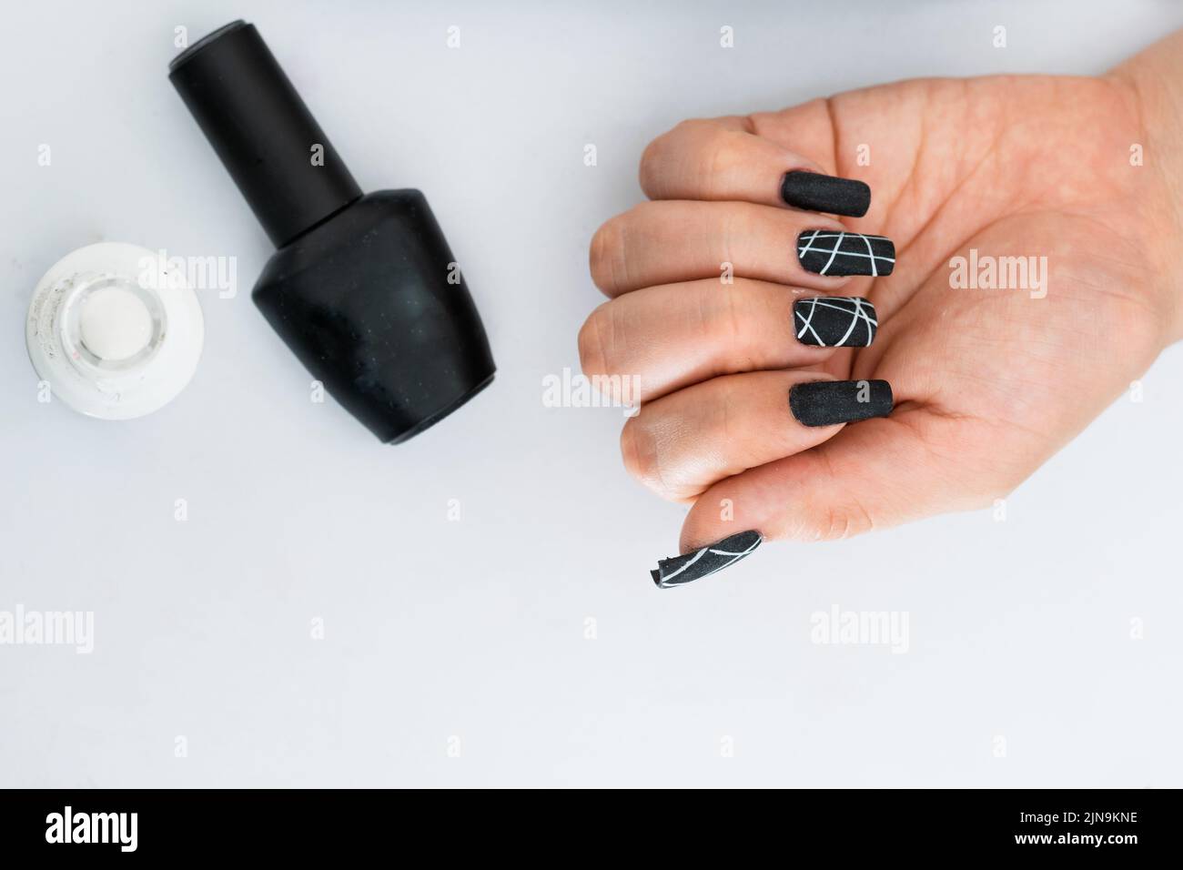mano di una ragazza latina, posta sul tavolo, ha le dita con le unghie dipinte di nero con strisce bianche accanto a loro un nero opaco smalto per unghie Foto Stock