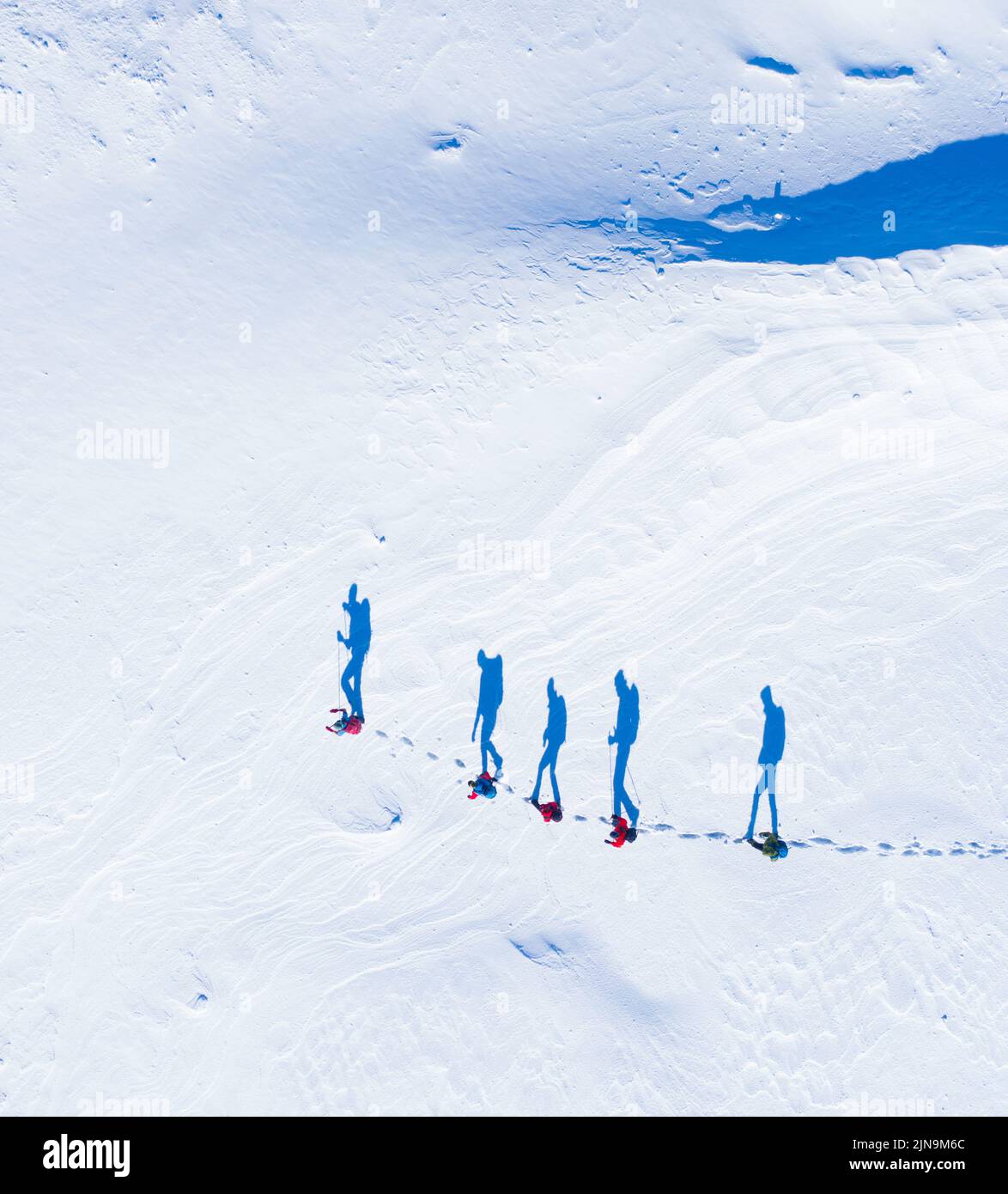 Un gruppo di escursionisti visti dall'aria con ombre che sembrano camminare nella neve in fila Foto Stock