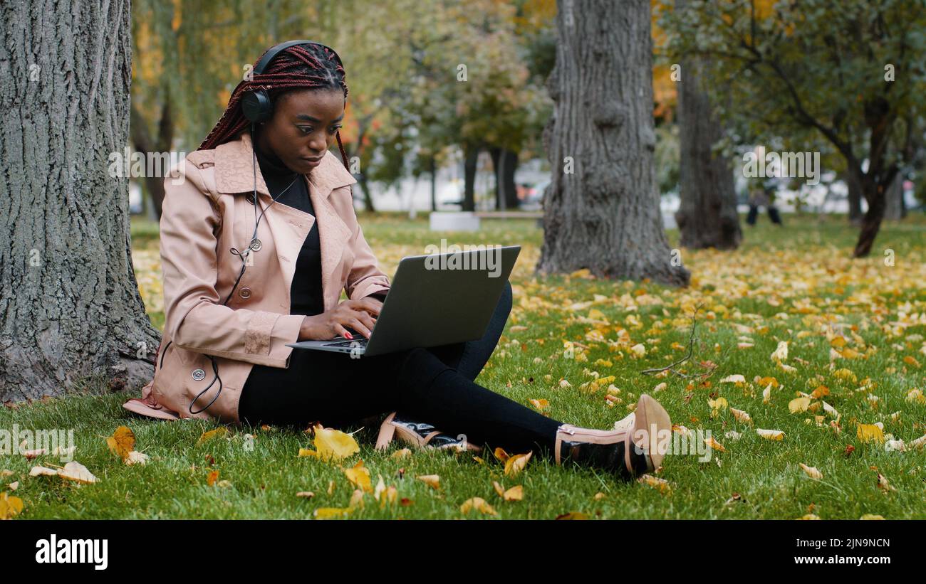 Giovane studentessa femminile focalizzata freelancer seduta in autunno parco vicino albero di lavoro su laptop digitando messaggio controlla e-mail studiando distanza remota online Foto Stock