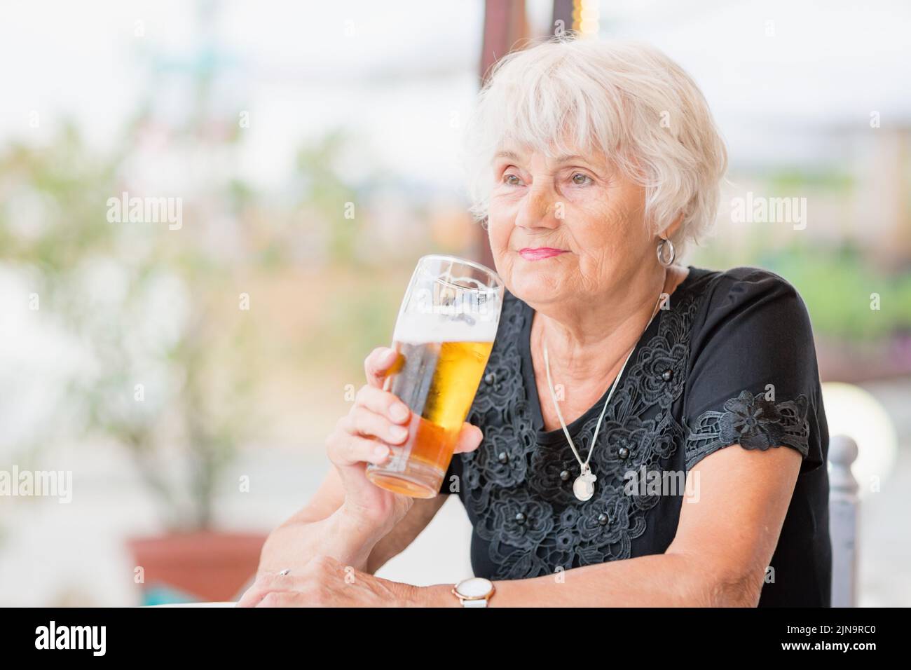 Donna matura seduta a un tavolo in un bar estivo e bere birra Foto Stock