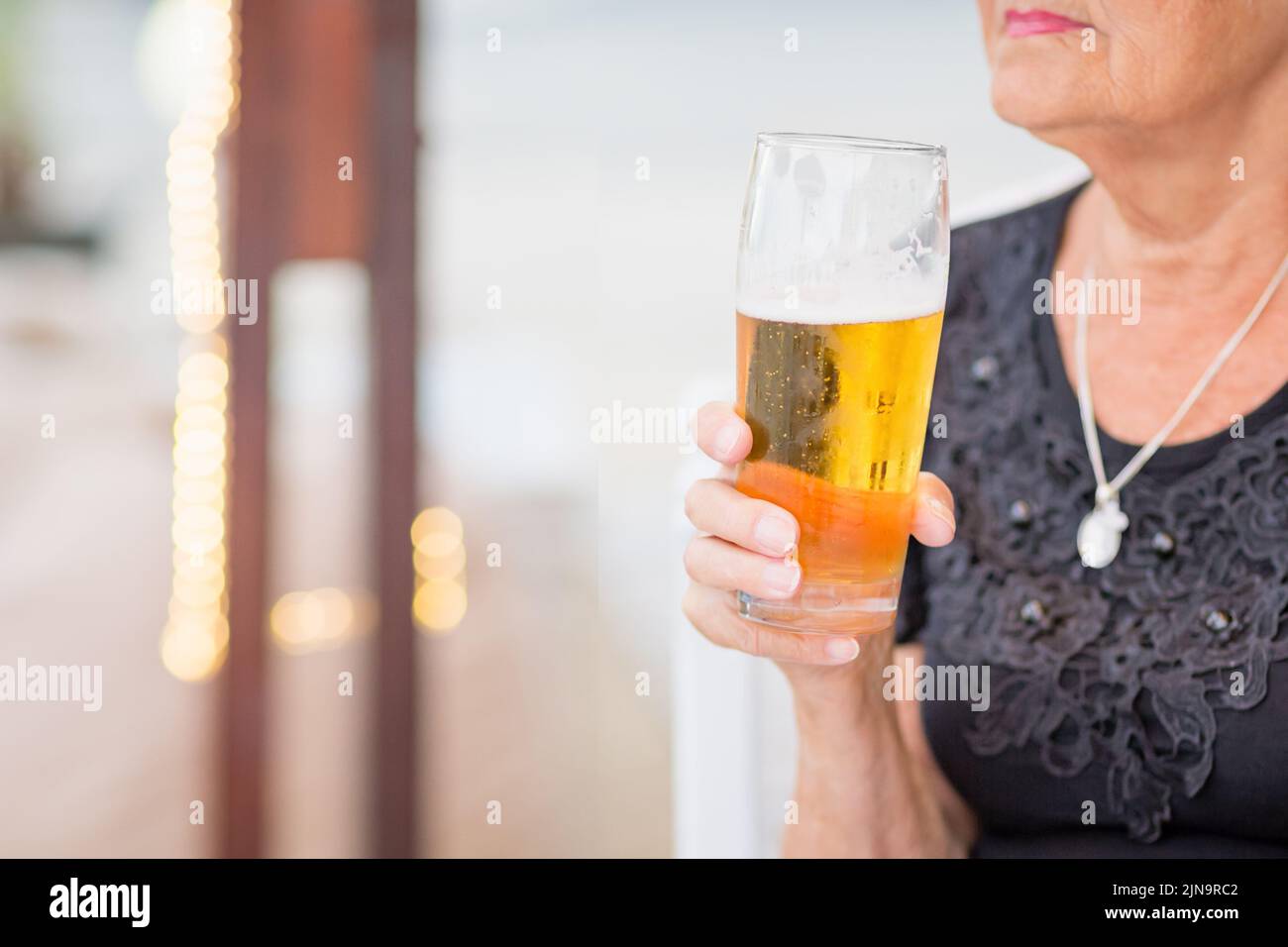 Donna matura seduta a un tavolo in un bar estivo e bere birra Foto Stock