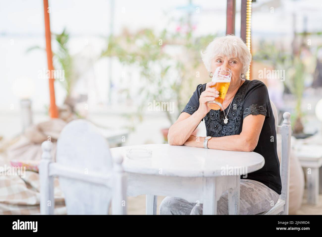 Donna matura seduta a un tavolo in un bar estivo e bere birra Foto Stock