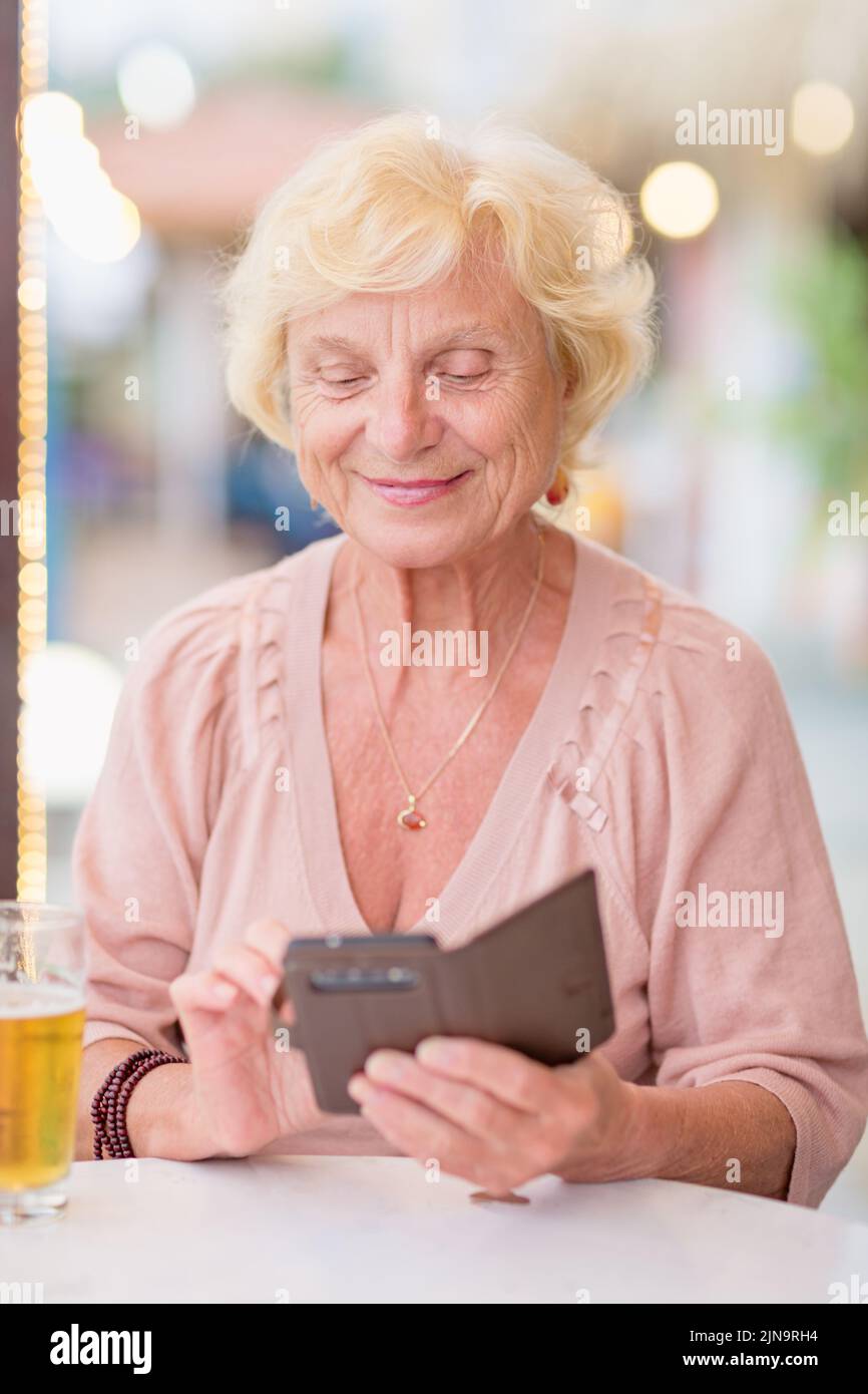 Donna matura seduta a un tavolo in un bar estivo e bere birra Foto Stock