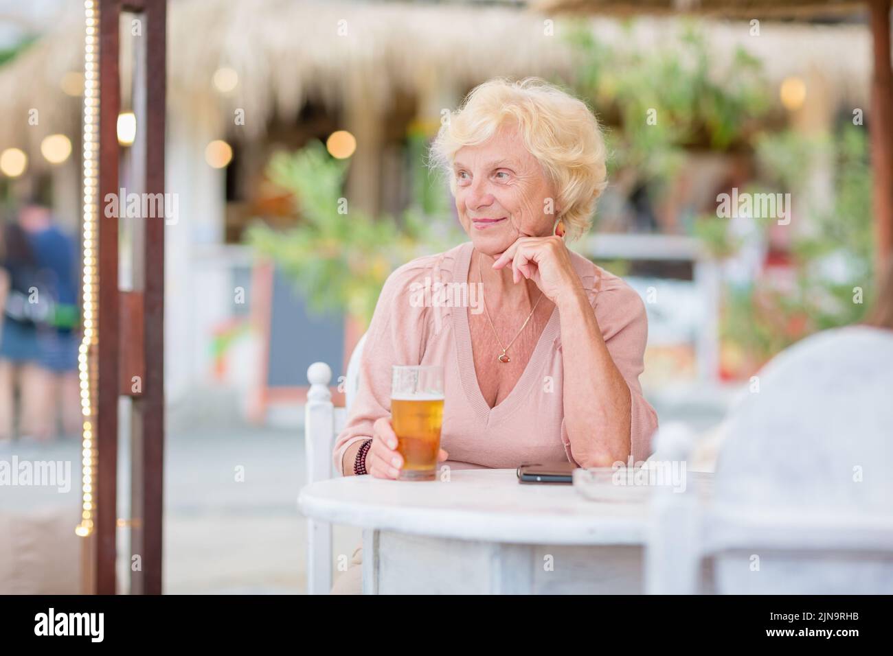Donna matura seduta a un tavolo in un bar estivo e bere birra Foto Stock