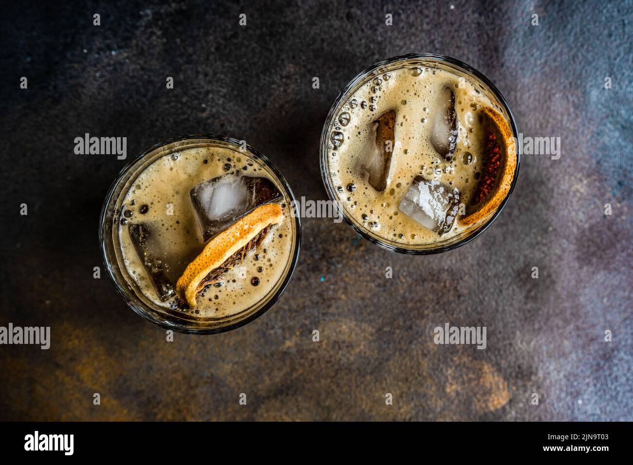 Cocktail alcolico con coke nel bicchiere con fetta di cubetti di arancio e ghiaccio su un tavolo di cemento scuro Foto Stock
