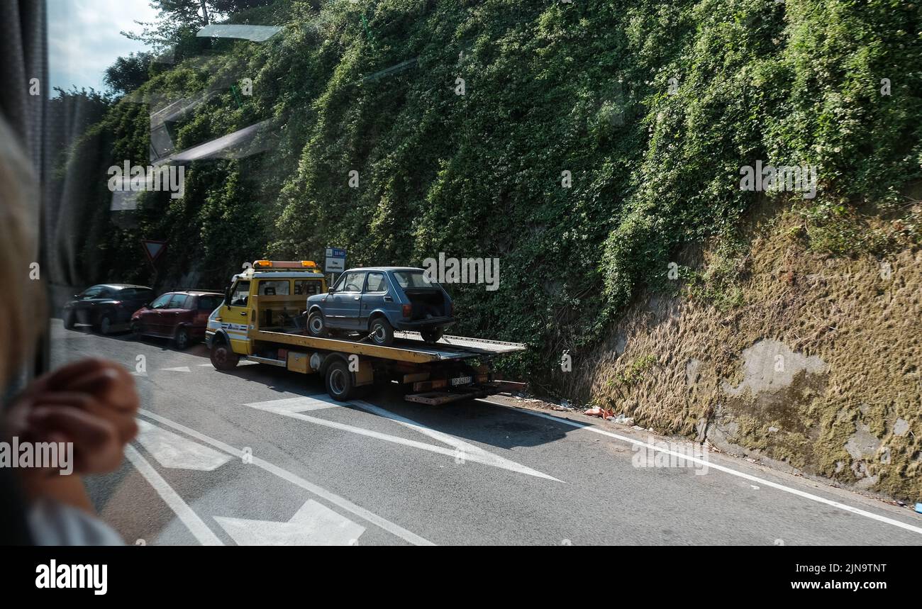 La Fiat 126 è scomposta sul retro di un camion di recupero in Italia visto da una vetrina di pullman con spazio di copia e dettaglio in primo piano. Foto Stock