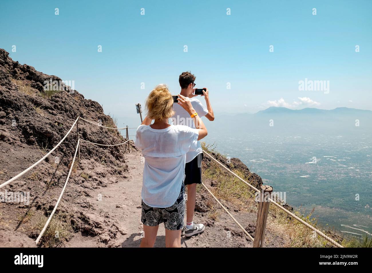 Una mamma e un figlio adolescente scattano foto sul loro cellulare della vista sul Vesuvio in Italia. Il vulcano attivo è alto oltre 1200 metri. Foto Stock