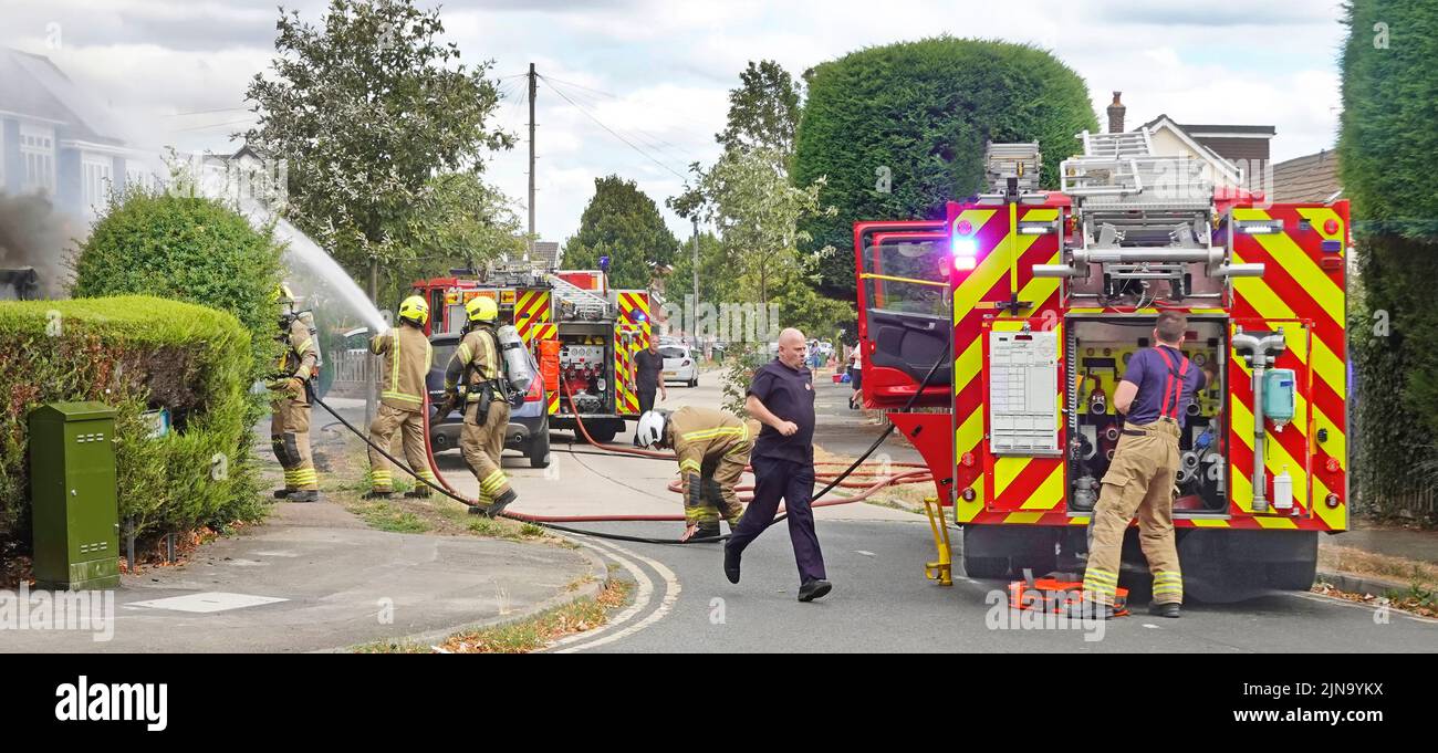 Servizio antincendio e di soccorso Essex vigili del fuoco vigili del fuoco che spruzzano acqua sul fuoco casa vista posteriore del motore di vigili del fuoco di brigata in strada residenziale Inghilterra Regno Unito Foto Stock