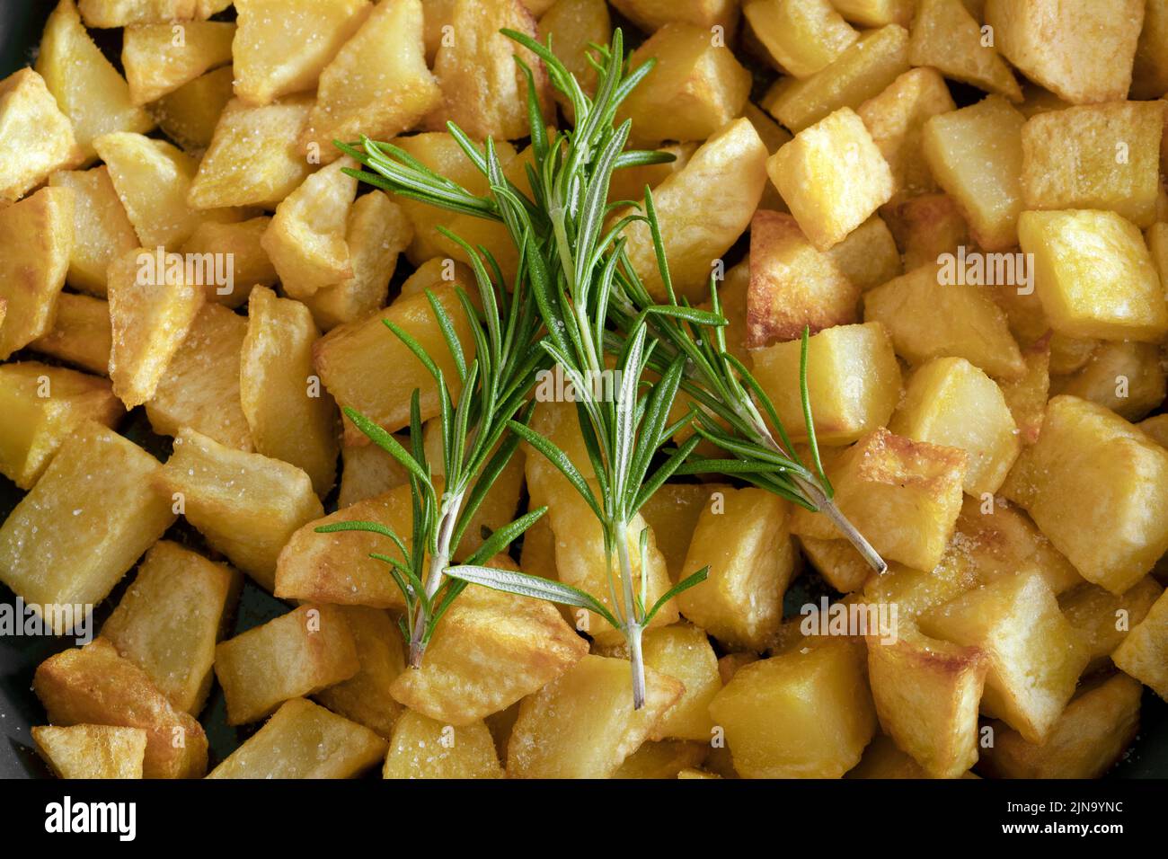 Macro primo piano di un rametto di rosmarino con patate fatte in casa sullo sfondo. Foto Stock