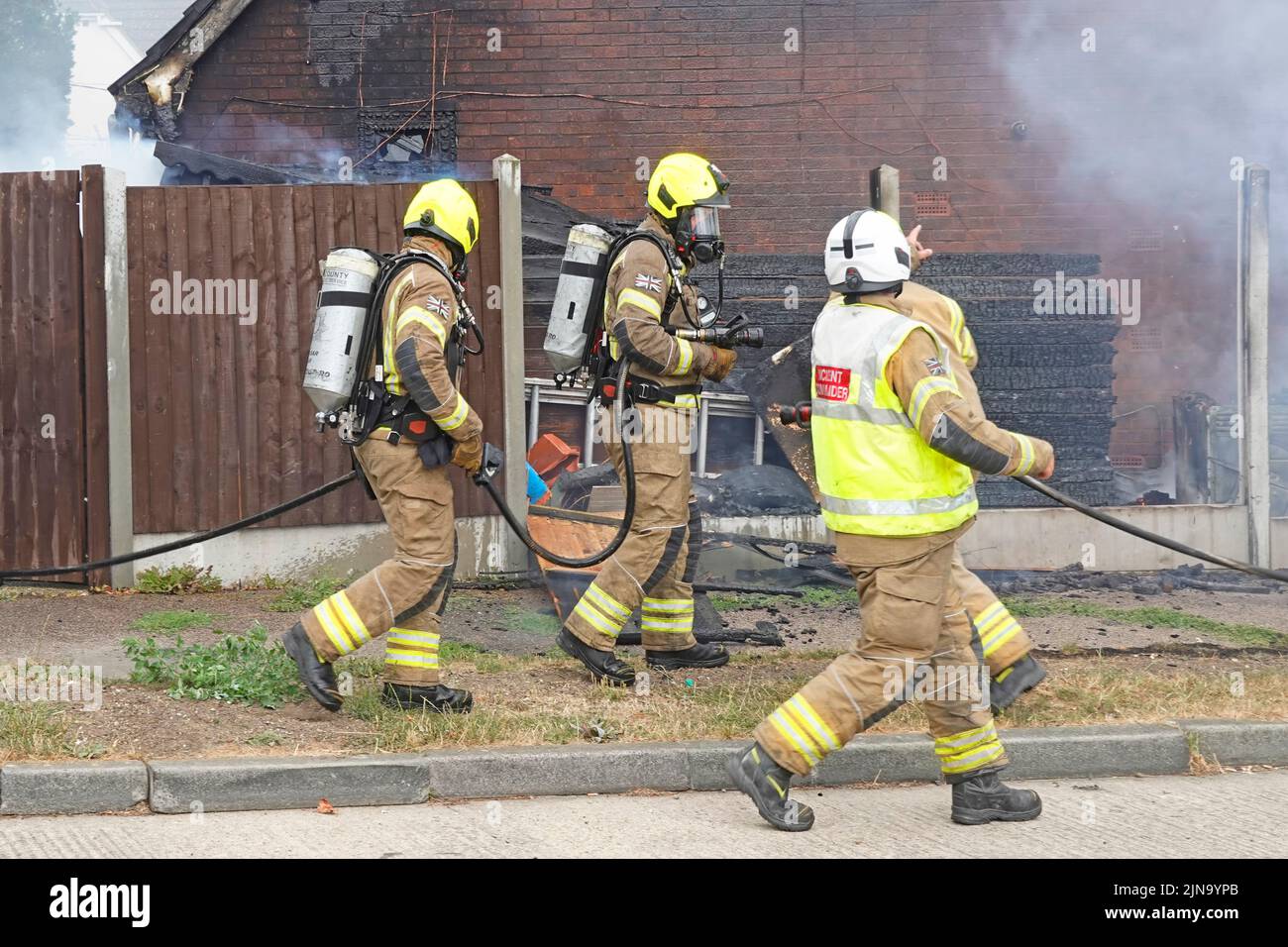 Due vigili del fuoco vigili del fuoco abbigliamento protettivo e apparecchi respiratori in procinto di cercare all'interno di casa bruciante edificio incendio Inghilterra UK Foto Stock