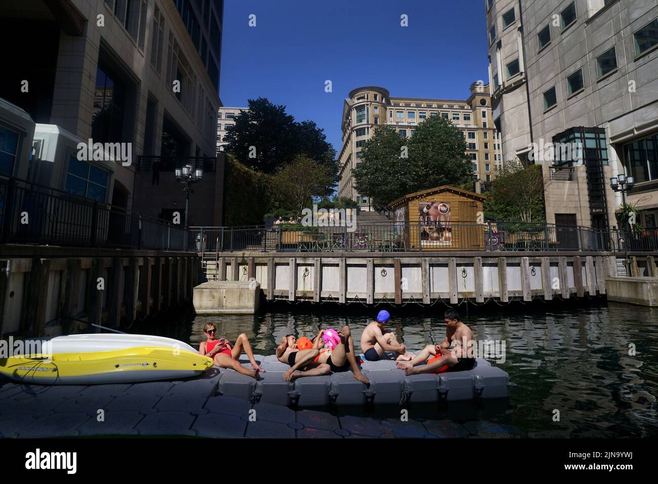 Un gruppo di nuotatori si prendere il sole accanto al nuovo luogo di nuoto all'aperto a Canary Wharf durante il clima caldo nella parte est di Londra. L'ufficio MET ha emesso un avvertimento color ambra per il calore estremo che copre quattro giorni da giovedì a domenica per alcune parti dell'Inghilterra e del Galles come nuovi telai ad onda calda. Data foto: Mercoledì 10 agosto 2022. Foto Stock