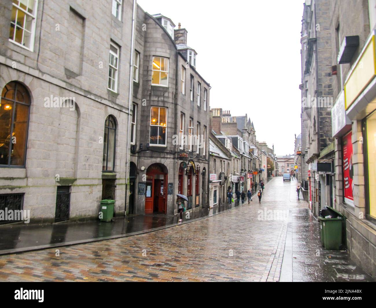 Guardando giù una stretta strada di mattoni, fiancheggiata da edifici di granito, ad Aberdeen, Scozia, bagnato dopo una rapida doccia a pioggia Foto Stock