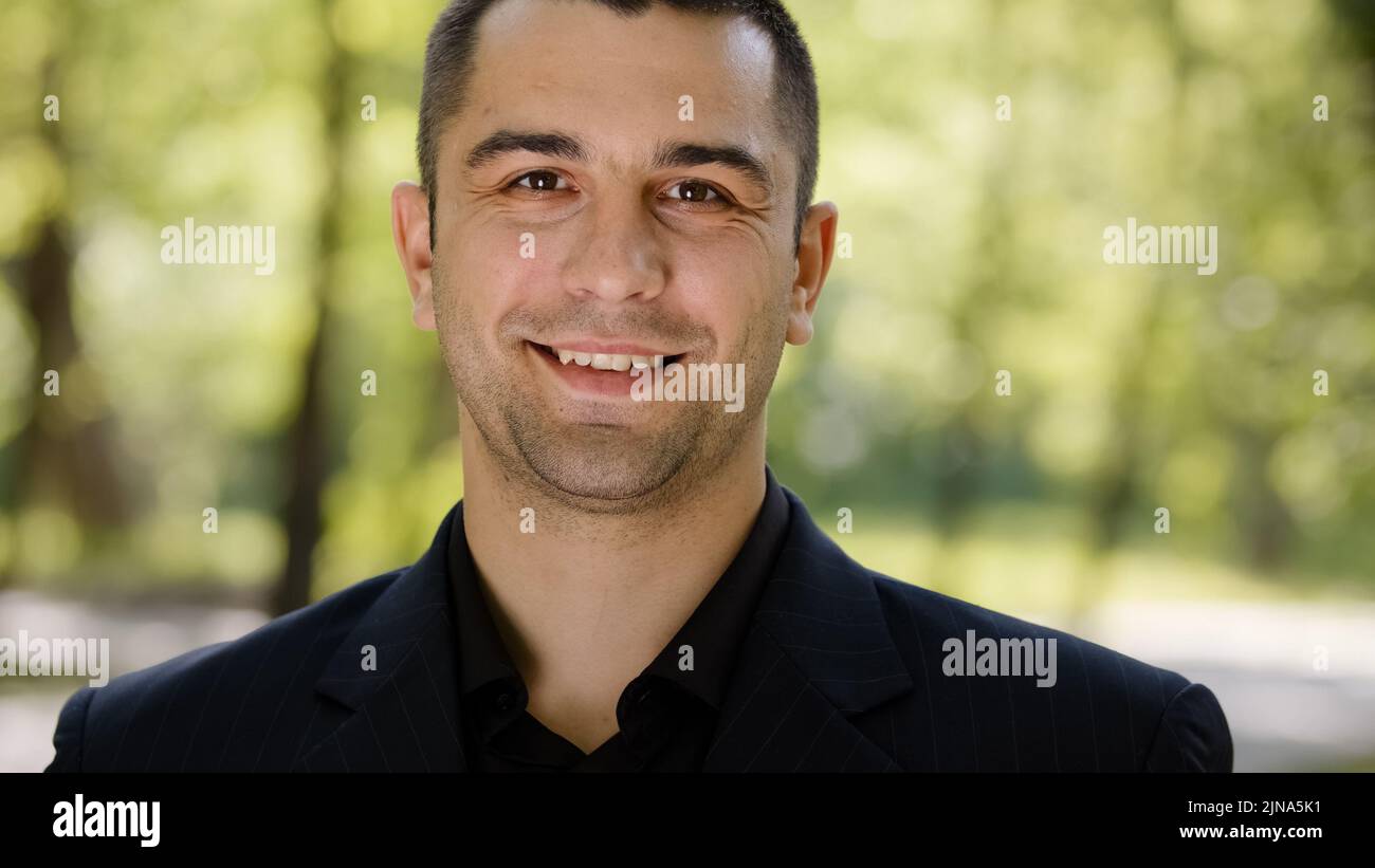 Outdoors ritratto di uomo adulto caucasico ragazzo felice maschio faccia riuscito uomo d'affari millenario indossa vestito nero girando testa guardando la macchina fotografica sorridente Foto Stock