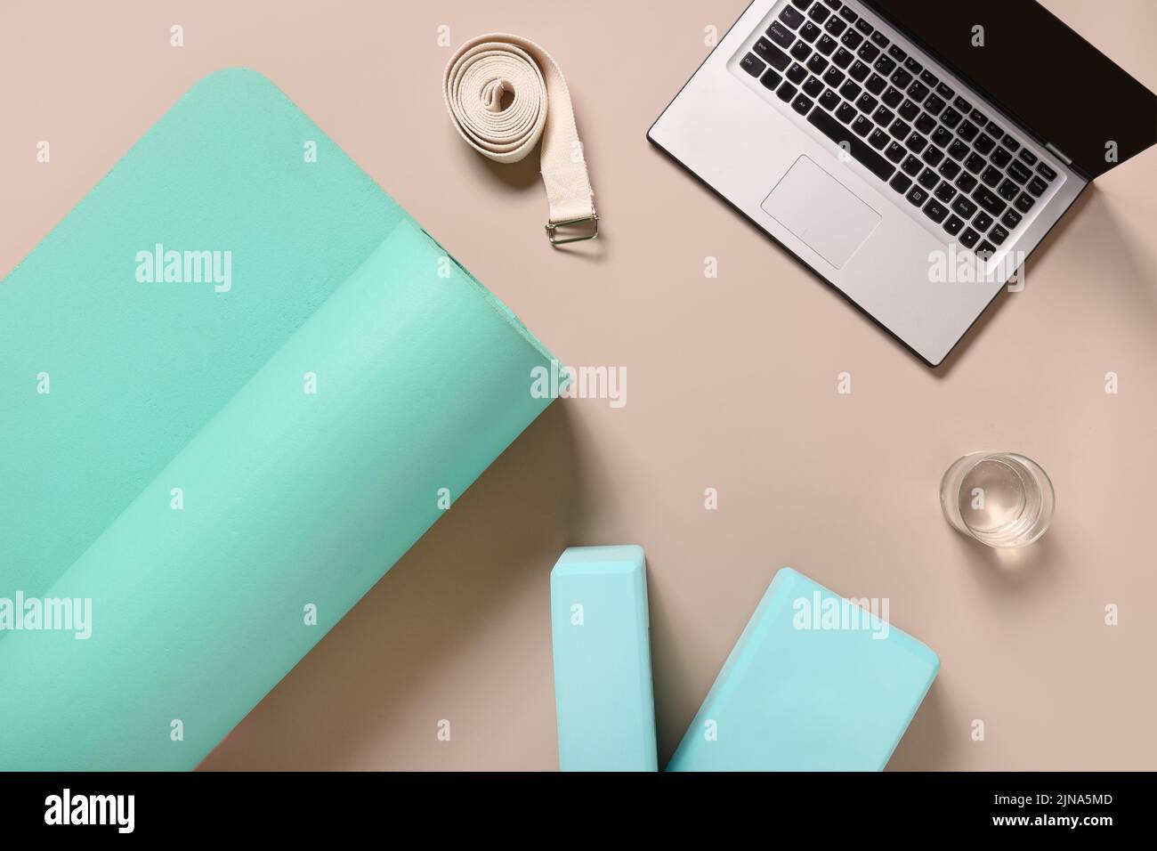 Yoga pratica, meditazione, apprendimento ed edicazione. Tappetino verde, due blocchi, acqua, orologio e cinturino bianco su sfondo beige. Vista dall'alto. Foto Stock