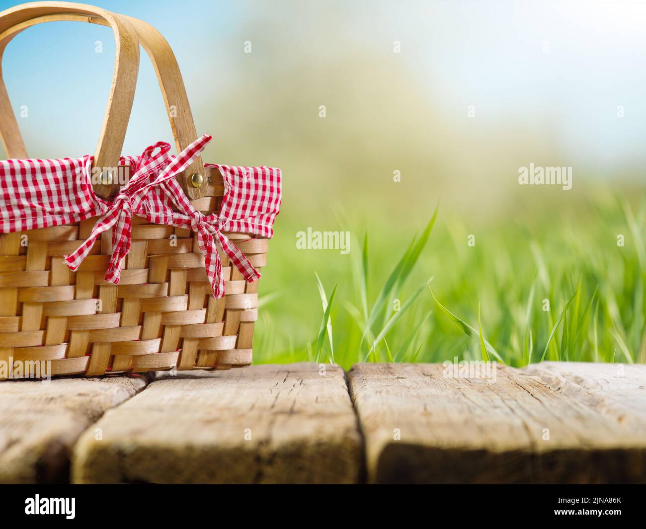 Sullo sfondo della natura estiva, erba verde, un cestino da picnic accogliente su un tavolo di legno. Campeggio, tradizioni familiari, pic-nic, stile di vita sano. T Foto Stock