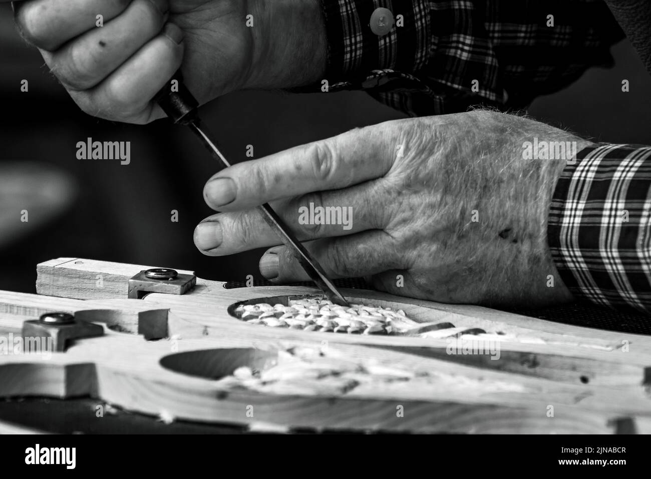 Primo piano delle mani maschili utilizzando una sgorbia per intagliare un disegno in legno. Foto Stock