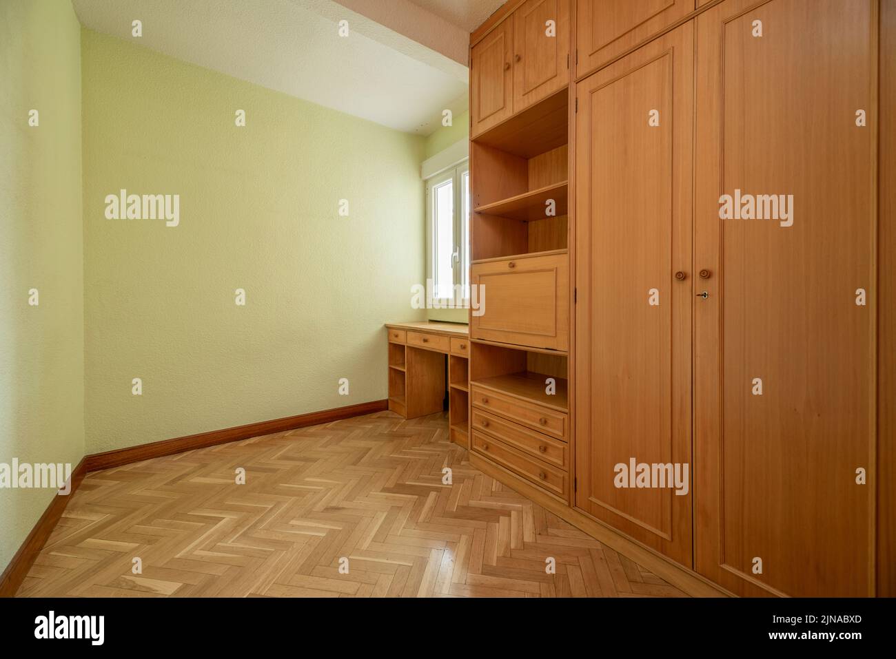 Camera da letto vuota con parquet di quercia a spina di pesce, armadi a muro, scrivania e cassettiera completamente ricoperta da pareti di legno chiaro e verniciata di verde chiaro Foto Stock