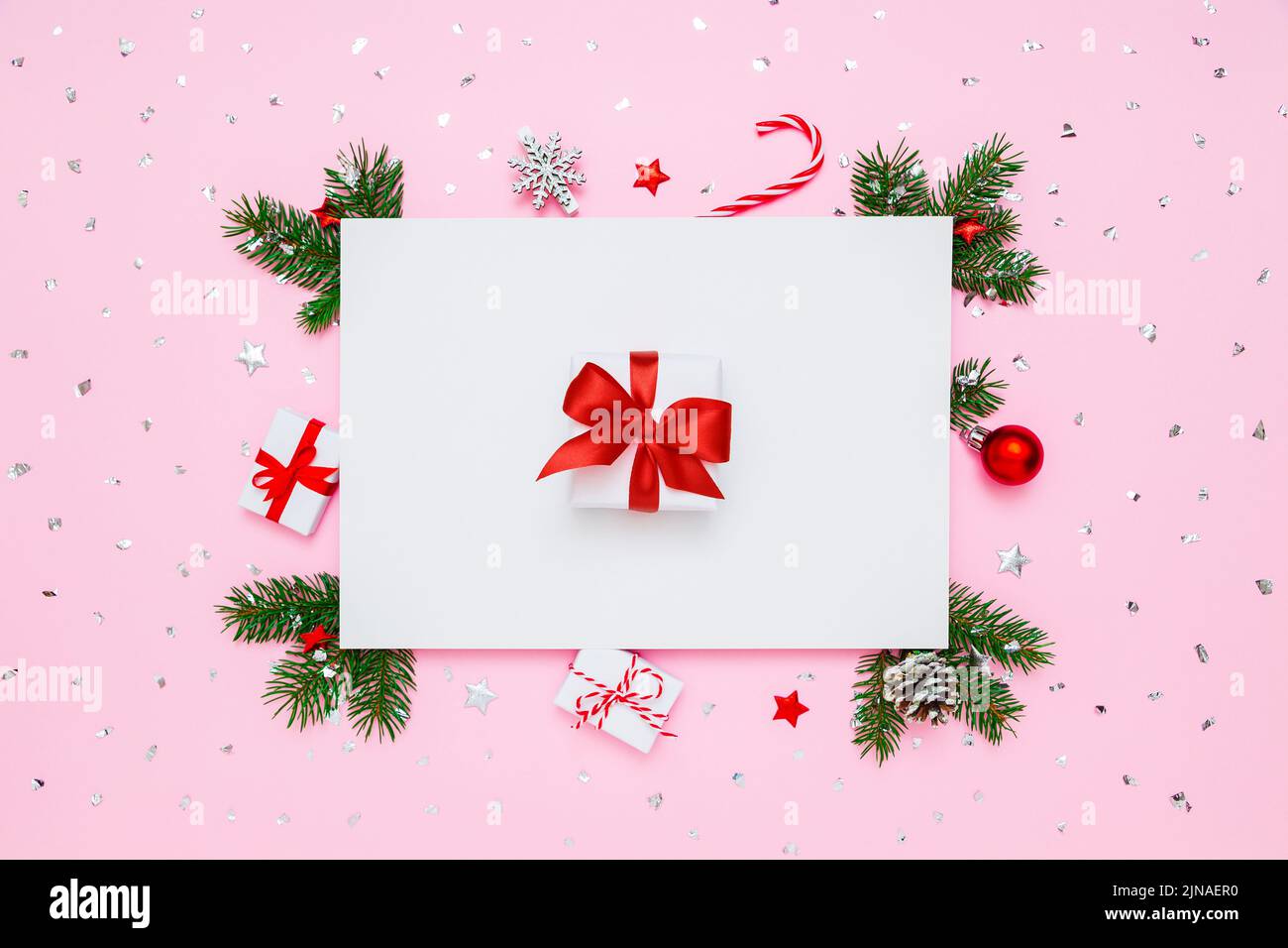 Natale, Capodanno disposizione vacanza. Scatola regalo bianca con arco rosso in cornice di rami di abete naturale e decorazioni su fondo piatto bianco e rosa pastello Foto Stock