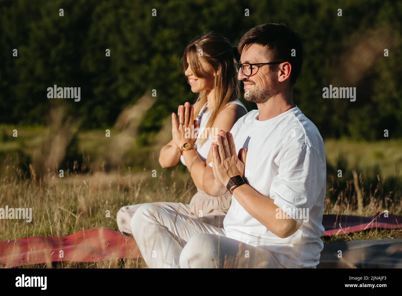 Giovane coppia di adulti meditando all'aperto nella natura, donna allegra e uomo felice che pratica lo Yoga Foto Stock