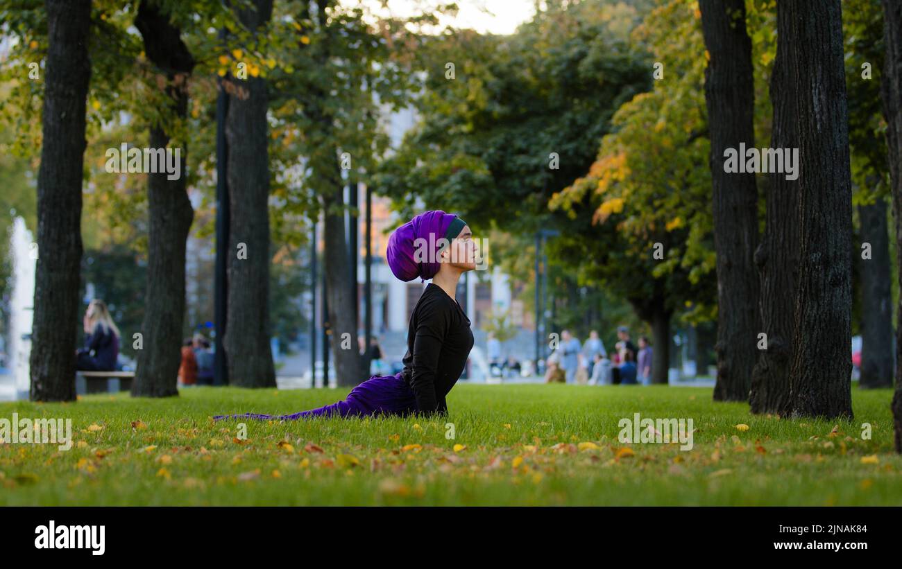 Donna atletica musulmana pratica yoga sole saluto in parco su erba mattina routine di fronte cane posa asana per la cura del corpo sano stretching spina dorsale Foto Stock